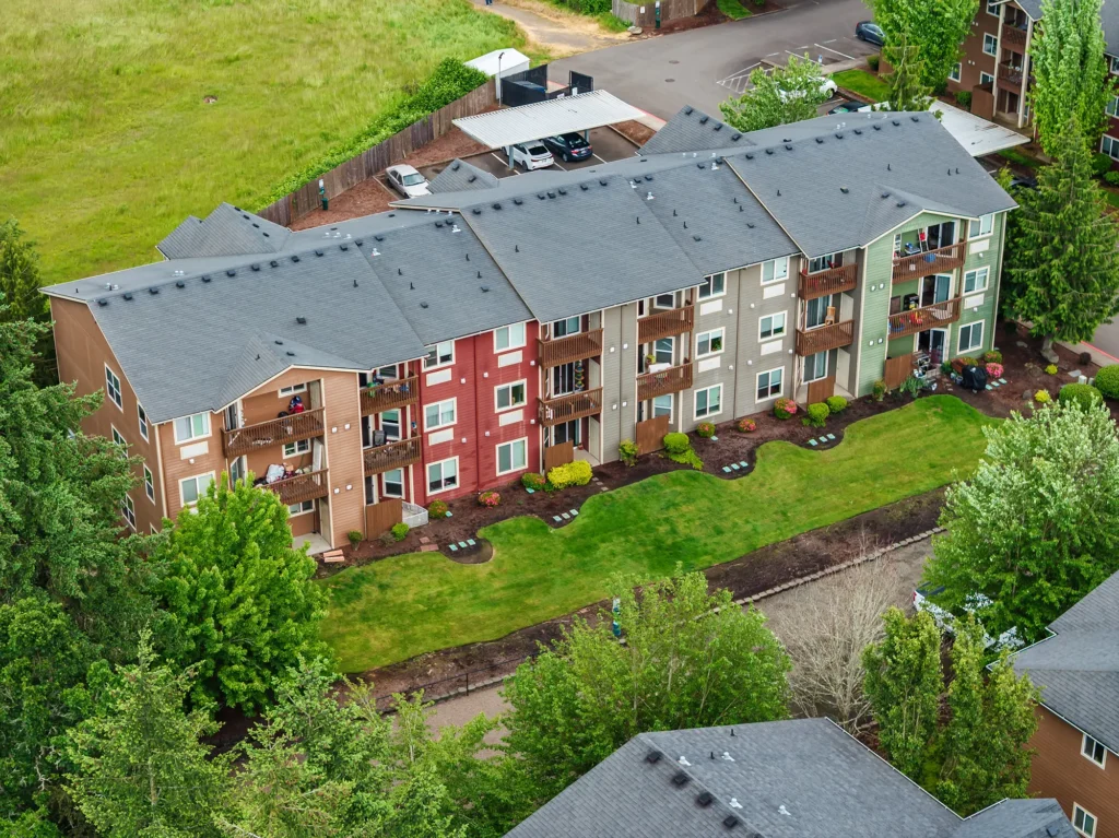 Aerial view of a colorful, three-story apartment building with red, beige, and green sections. Well-maintained lawn and vibrant trees surround the area.