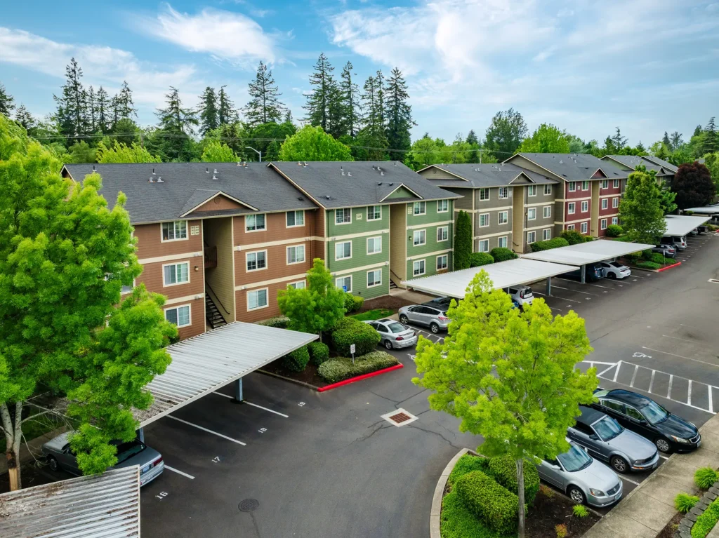 Aerial view of a row of colorful, three-story apartment buildings with carports, surrounded by trees.