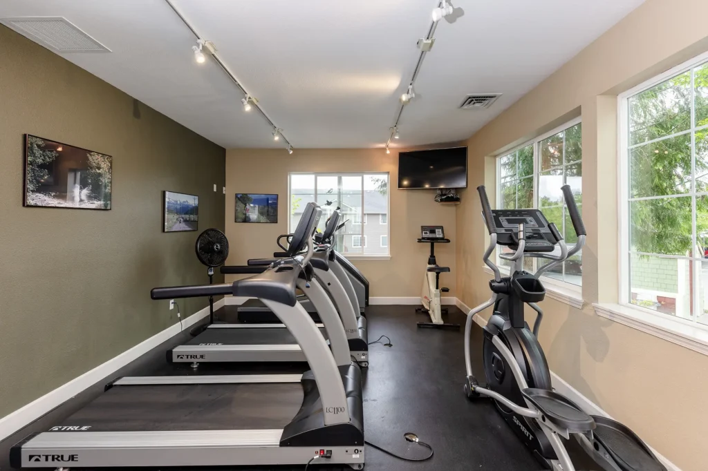 Compact gym room with treadmills and an elliptical machine facing a wall-mounted TV.