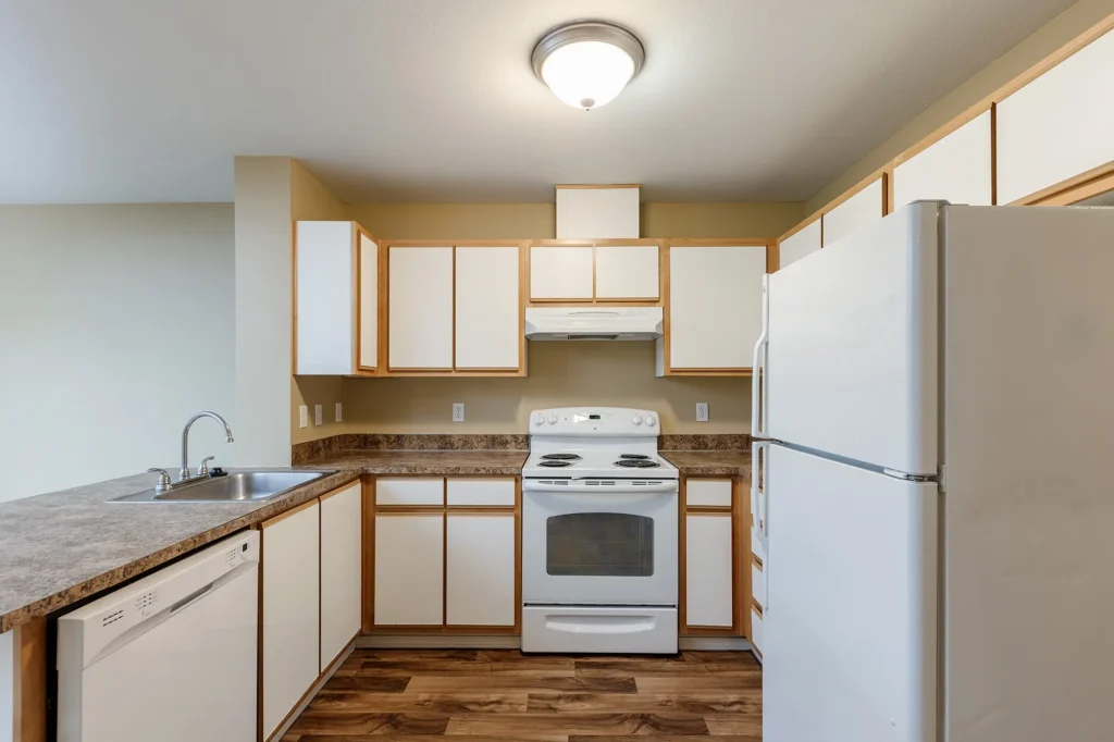 Kitchen with white cabinets, white appliances, and wood flooring. Includes a stove, dishwasher, and fridge.