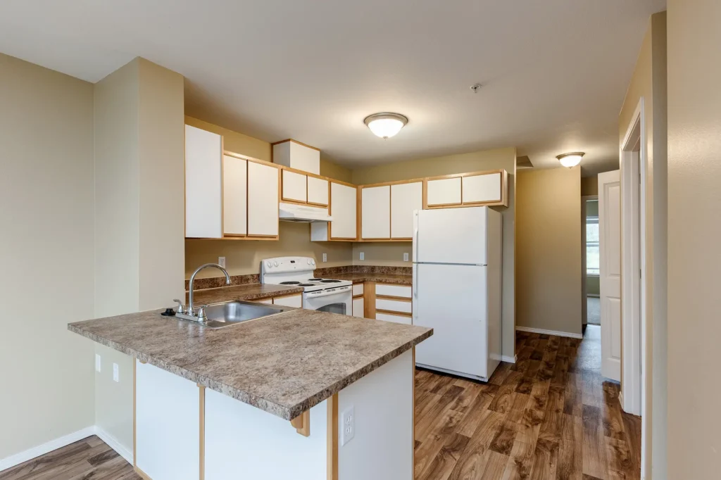 Kitchen with white cabinets, white appliances, and wood flooring. Includes a stove, dishwasher, and fridge.