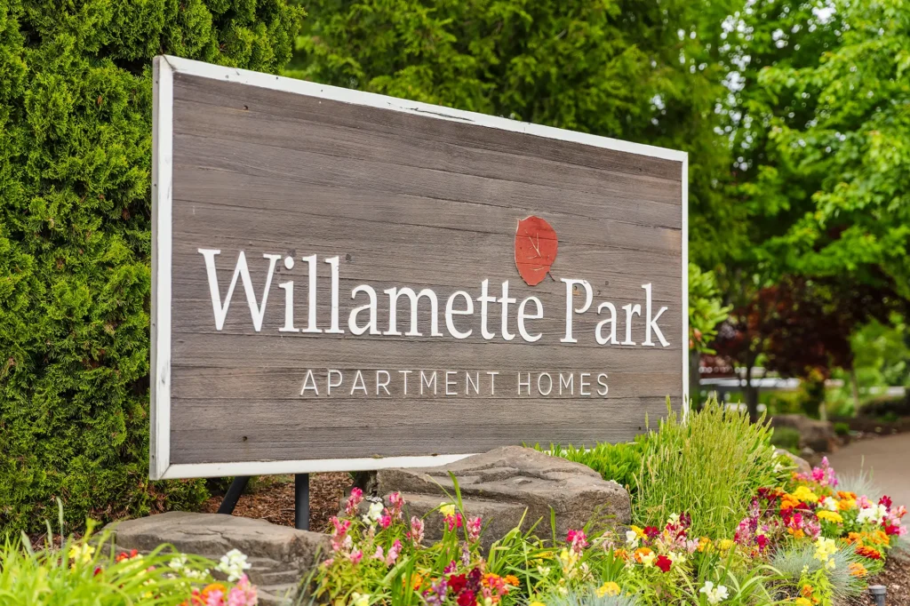 Exterior sign next to lush landscaping with the words 'Willamette Park Apartment Homes'.