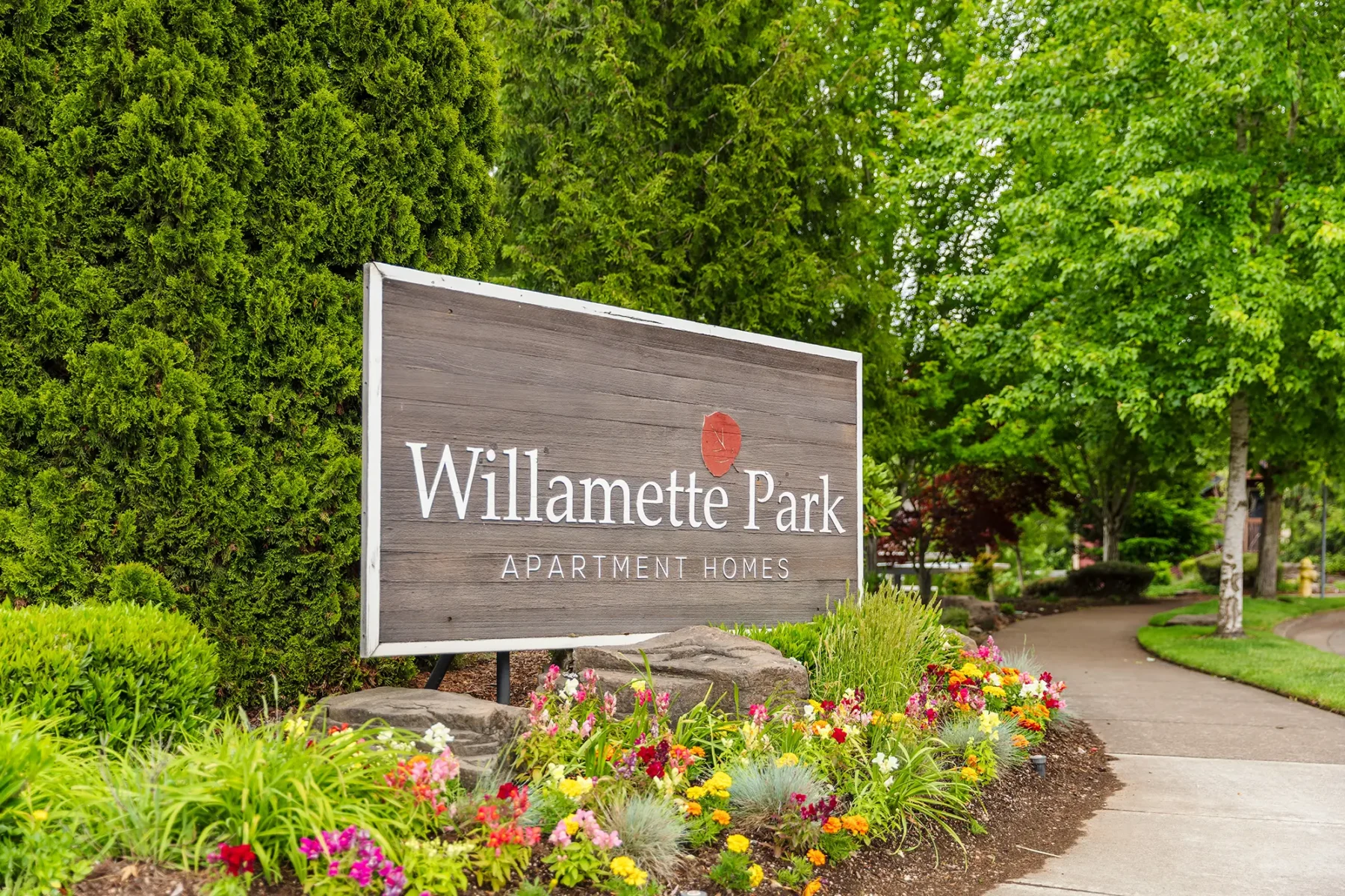 Exterior sign next to lush landscaping with the words 'Willamette Park Apartment Homes'.