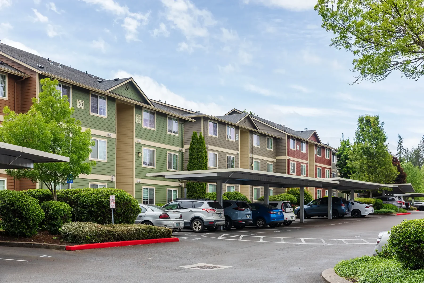 Suburban apartment complex with colorful buildings, covered parking, and several cars.