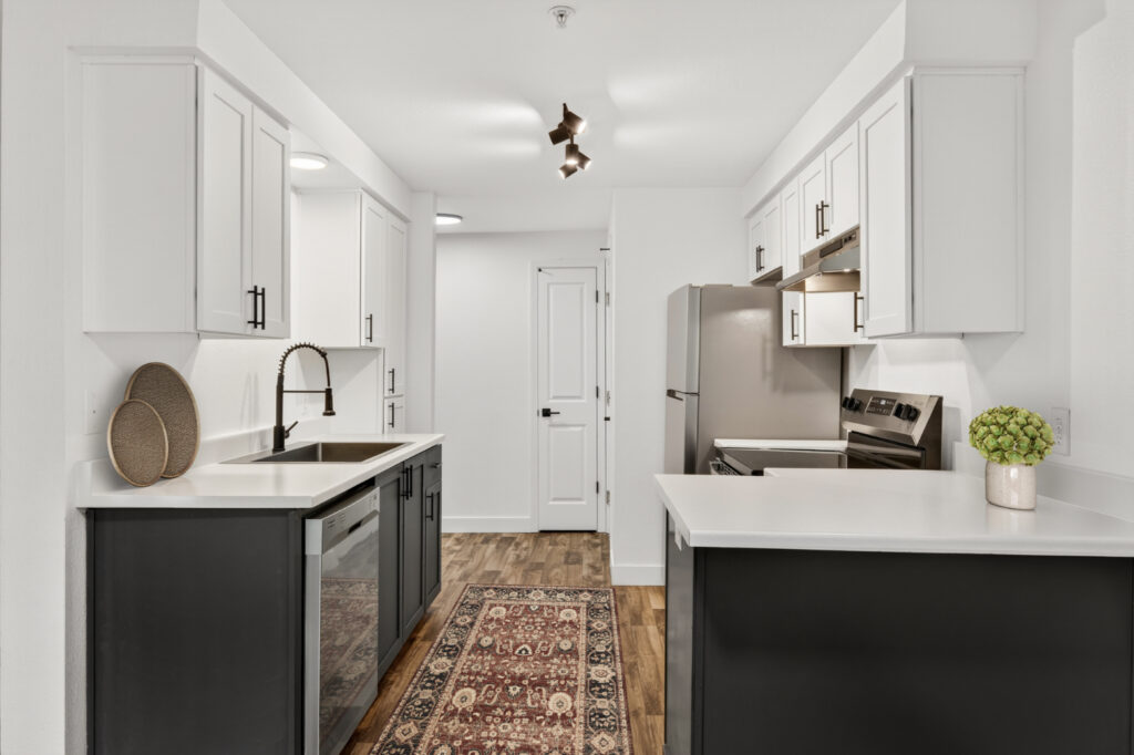 Modern kitchen with white cabinets, black lower cabinets, stainless steel appliances, under-cabinet lighting, a patterned rug on wood flooring, and a center sink with a black faucet.